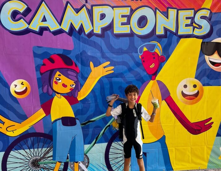 Mateo poses after his triathlon in front of a congratulations banner