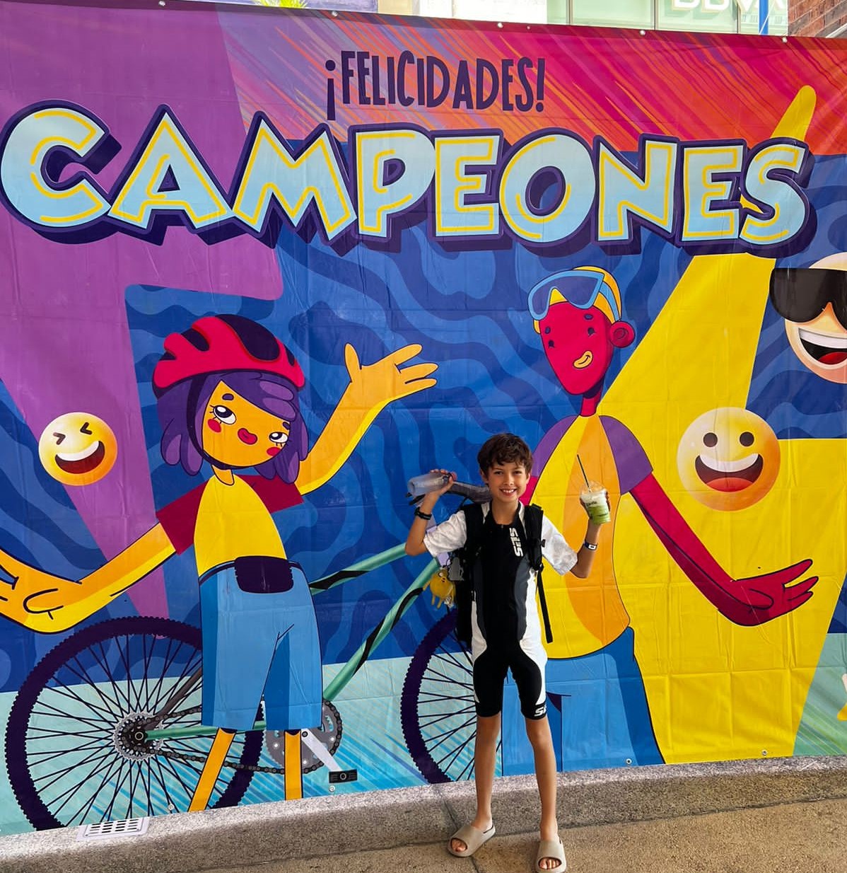 Mateo poses after his triathlon in front of a congratulations banner